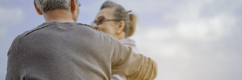 Ein älteres Paar sitzt gemeinsam am Strand und hält sich im Arm.