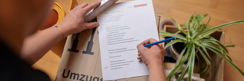 Mann hakt Umzugs-Checkliste auf Umzugskarton ab