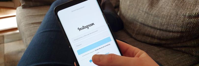 Foto aus der Perspektive einer Person, die auf einer Couch liegt und ein Smartphone in der Hand hält, das die Login-Seite von Instagram zeigt