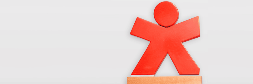 Bundespreis der Stiftung Verbraucherschutz: Ein rote Figürchen, das die Arme wegstreckt und auf einem Holzsockel befestigt ist