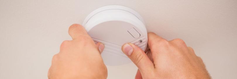 Zwei Hände arbeiten an einem Rauchmelder an der Decke