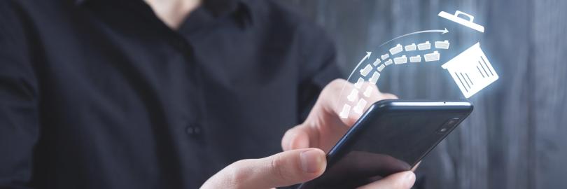 Ein Mann in einem schwarzen Hemd hält ein Smartphone in den Händen. Über dem Display schwebt eine digitale Illustration, die zeigt, wie mehrere Aktenordner-Symbole in einen Papierkorb fliegen, was den Vorgang des Löschens oder Aufräumens von Daten symbolisiert.