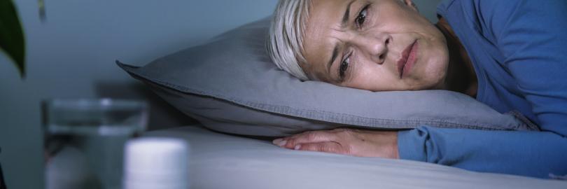 Eine schlaflose Frau liegt wach im Bett und schaut auf eine Dose mit Schlaftabletten
