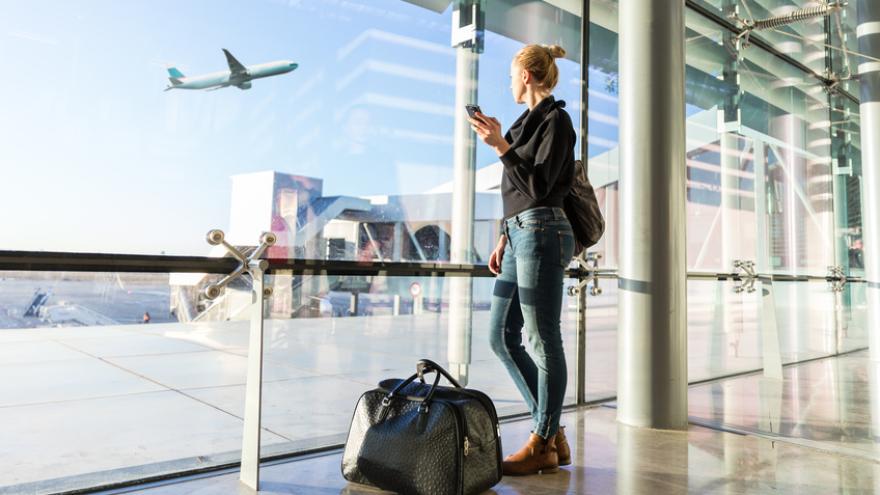 Frau schaut am Flughafen auf startendes Flugzeug