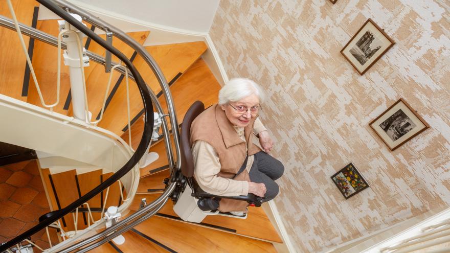 Eine ältere Dame fährt im Treppenhauf mit einem Treppenlift