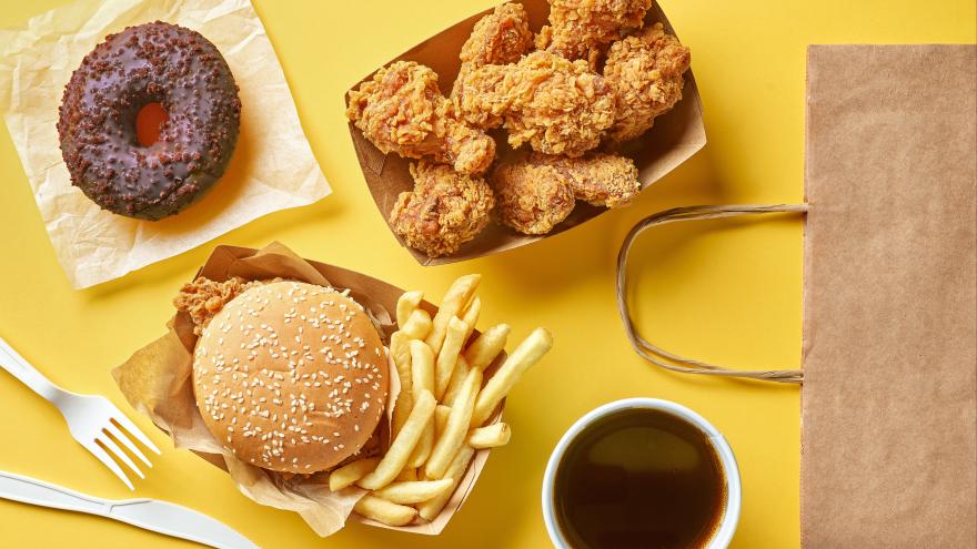 Fast Food Produkte Pommer, Burger und Donut in Einwegverpackungen auf einem gelben Tisch