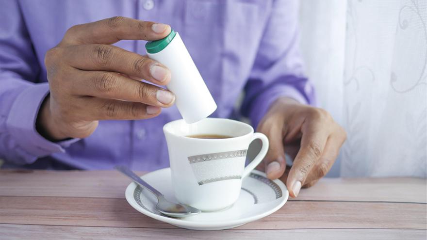 Ein Mann süßt Kaffee mit Süßstoff.