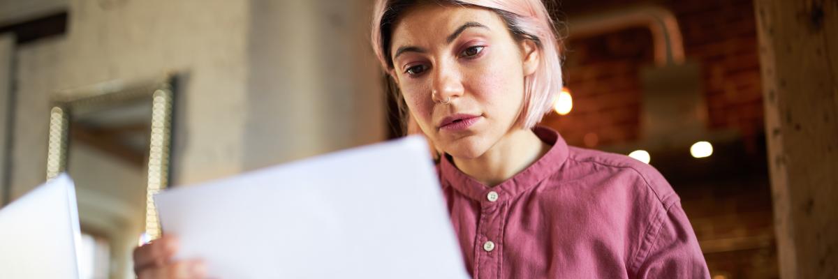 Eine junge Frau hält mit besorgtem Gesicht einen Brief in der Hand und liest 