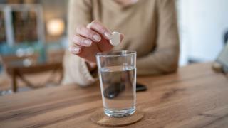 Eine Frauenhand hält eine weiße Tablette über ein Wasserglas