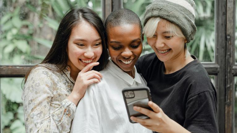 Drei Frauen, die lächelnd auf ein Smartphone schauen